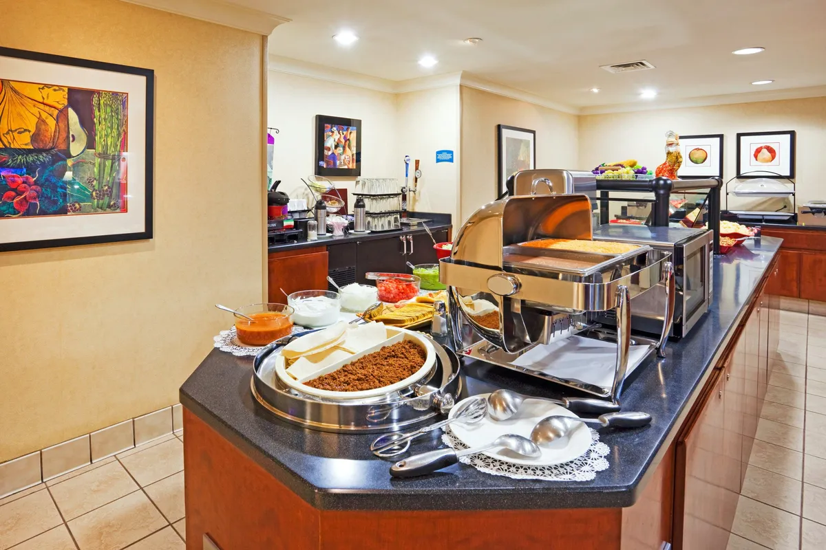 This image shows a buffet setup with decorative food containers, framed artwork, and guests sampling the morning spread. The atmosphere is casual and inviting, highlighting the communal feel of breakfast time at the property.
