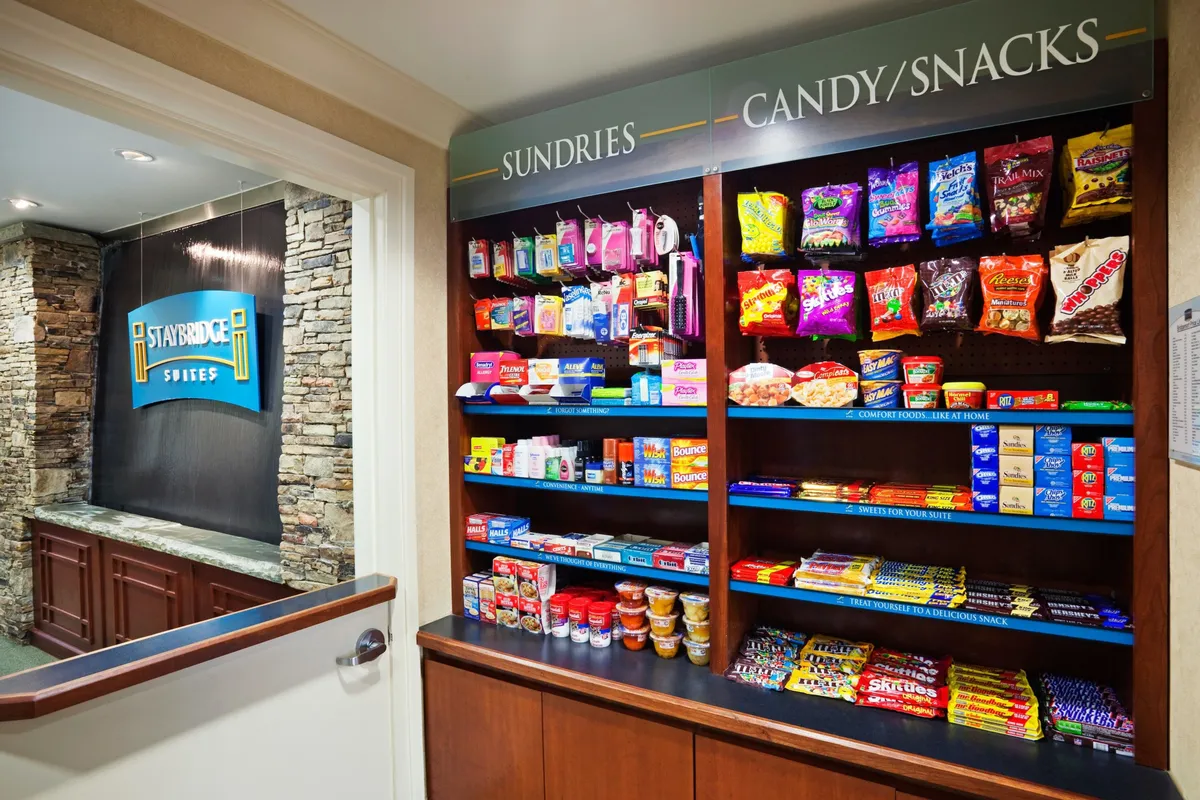 A conveniently located shelf of snacks and sundries sits adjacent to a stone feature wall and a casual reception counter. The space is casual, accessible, and designed to meet the everyday needs of travelers.