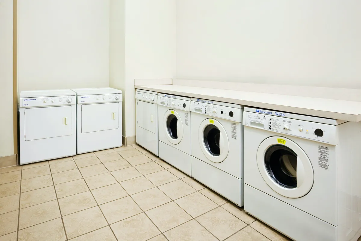 A practical, clean laundry room with several front-loading washing machines and dryers, along with ample counter space for folding clothes. The organized layout conveys ease and convenience for guests handling laundry during their stay.
