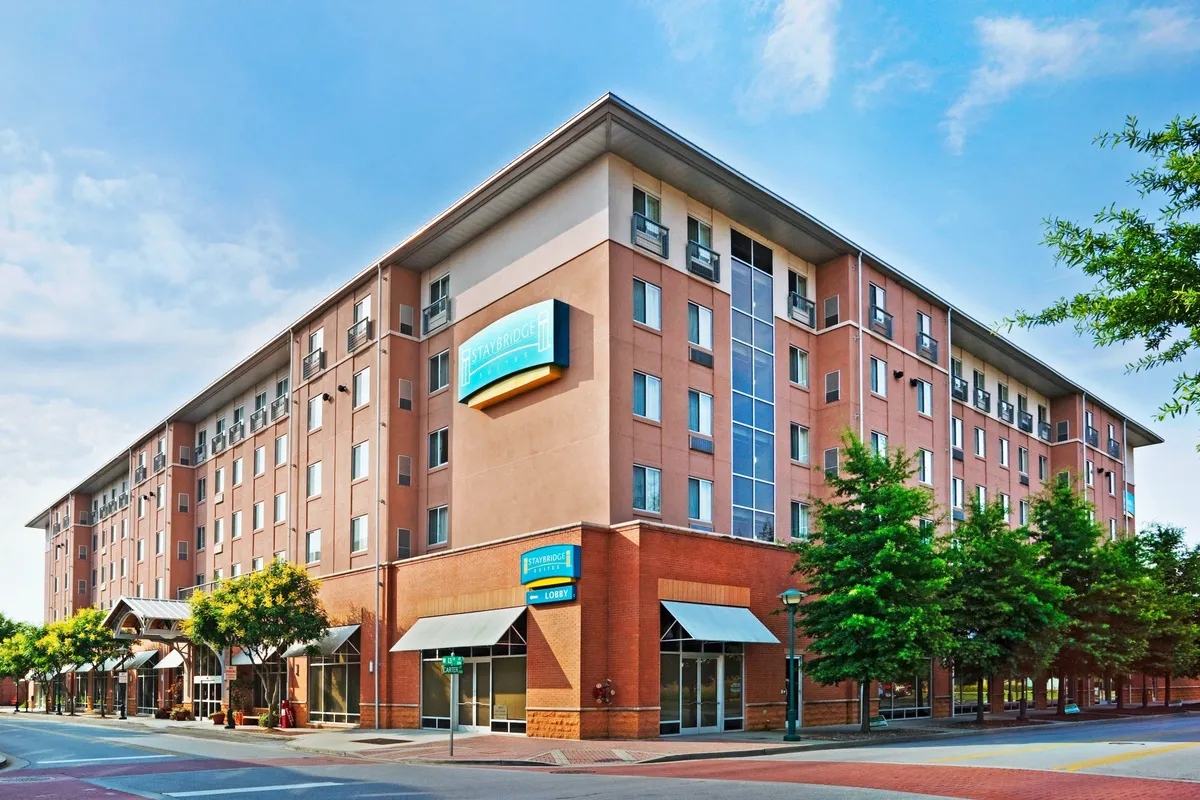 This image captures the hotel’s exterior facade, including the welcoming lobby entrance and tree-lined street. Guests can be seen arriving or strolling nearby, with the vibrant downtown neighborhood visible beyond. The inviting atmosphere and surrounding urban environment underline how the hotel is nestled within Chattanooga's bustling downtown.