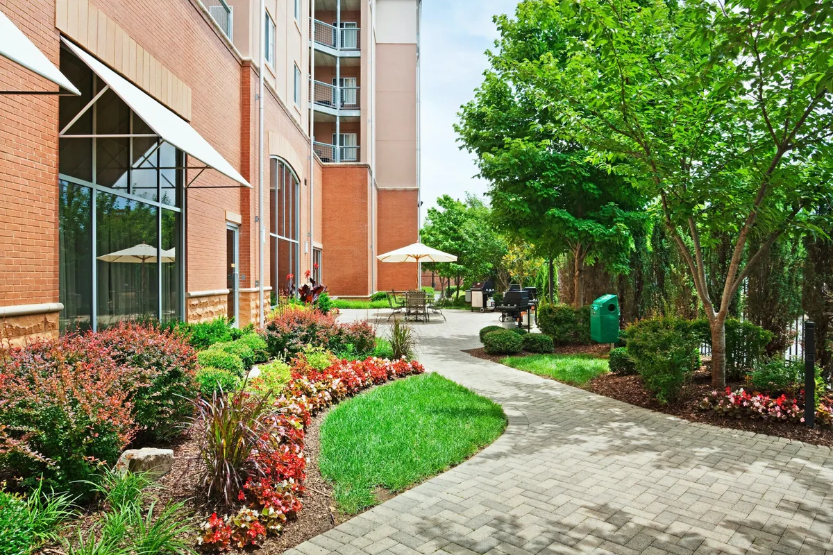 This exterior image features vibrant flower beds lining a winding pathway, with inviting outdoor seating nestled amidst lush greenery. The scene is bathed in natural light, creating a welcoming and peaceful atmosphere that encourages relaxation and connection with the outdoors.